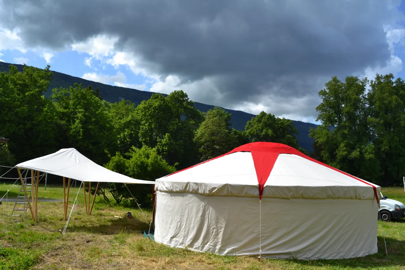 Yourte à toit conique rouge et blanc, dans un pré au pied des montagnes